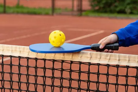 Une balle de pickle ball sur une raquette de pickle ball sur un filet de pickle ball